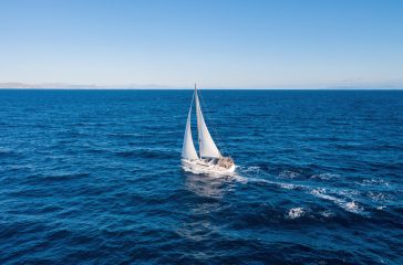 Sailing boat with white sails, cloudy sky and rippled sea background Sailing. Sailboat with open white sails, blue sky and sea, windy day. Summer vacation in Mediterranean sea Greece